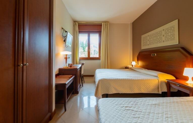 Camera d'hotel con due letti, scrivania e finestra con tende gialle.