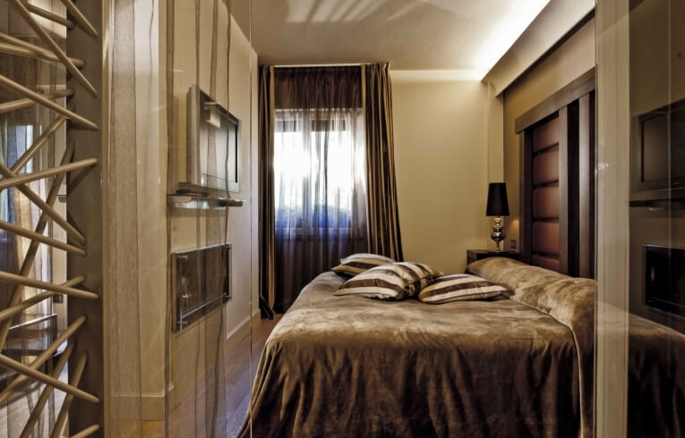 Camera d'hotel con letto, televisore, tende e lampada da comodino.