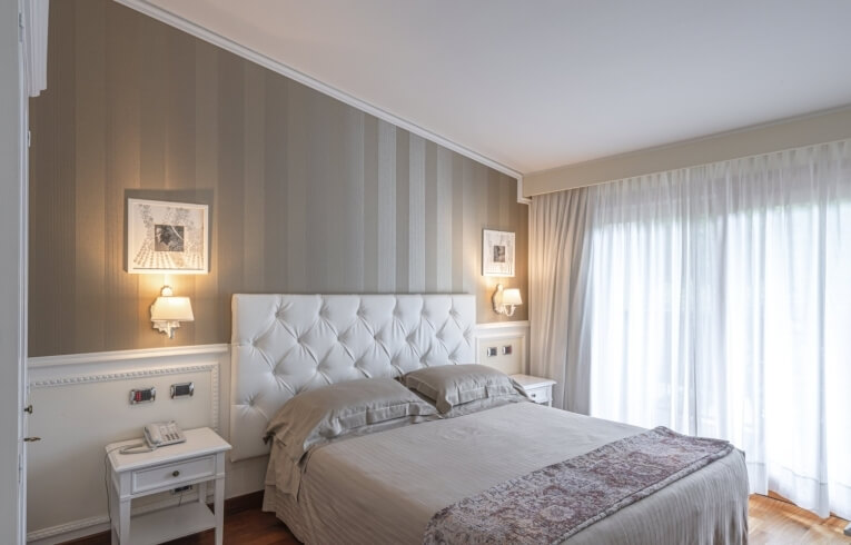 Hotelzimmer mit Bett, Nachttisch, Kunst und gestreiften Wänden.