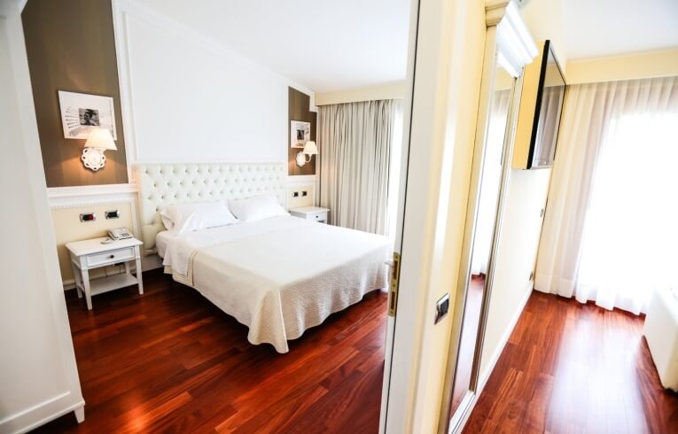 Helles Hotelzimmer mit Bett, Nachttisch, Fernseher und Kunstwerken.