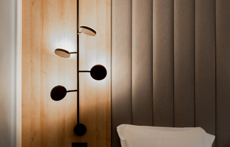 Wall-mounted light fixture with black stem on wood-paneled wall.