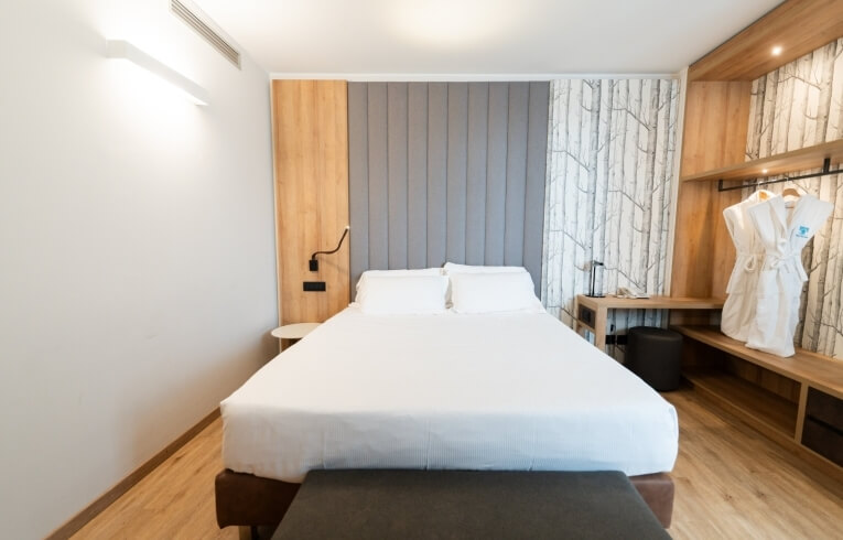 Hotel room with a bed, padded headboard, and hanging robes.