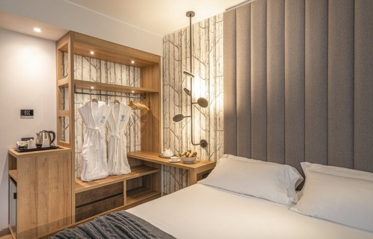 Hotel room with a bed, wardrobe, kettle, and patterned wallpaper.