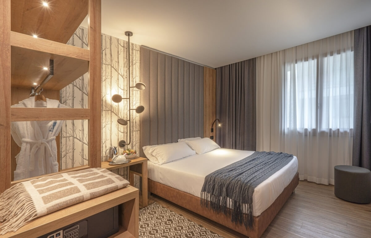 Camera d'hotel con letto, armadio, comò e finestre con tende.