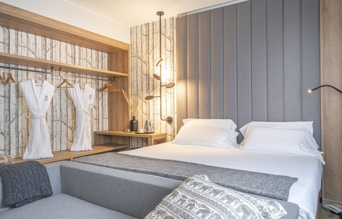 Camera d'hotel con letto bianco, divano grigio e decorazioni moderne.
