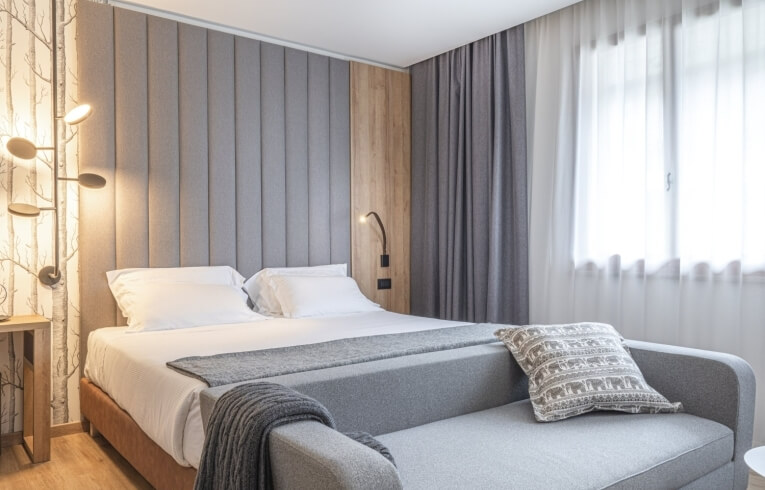 Helles Hotelzimmer mit Bett, Sofa und grauen Vorhängen.