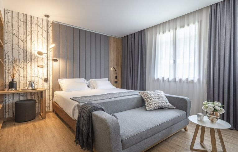 Hotelzimmer mit Bett, Sofa, Fenster und Tisch, Holzfußboden.