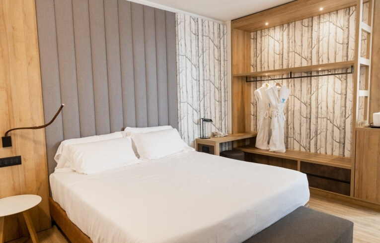 Cozy hotel room with bed, desk, wardrobe, and tree motif wallpaper.