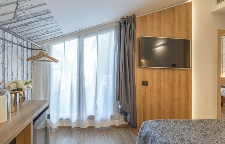 Hotel room with TV, curtains, dresser, flowers, and patterned bed.