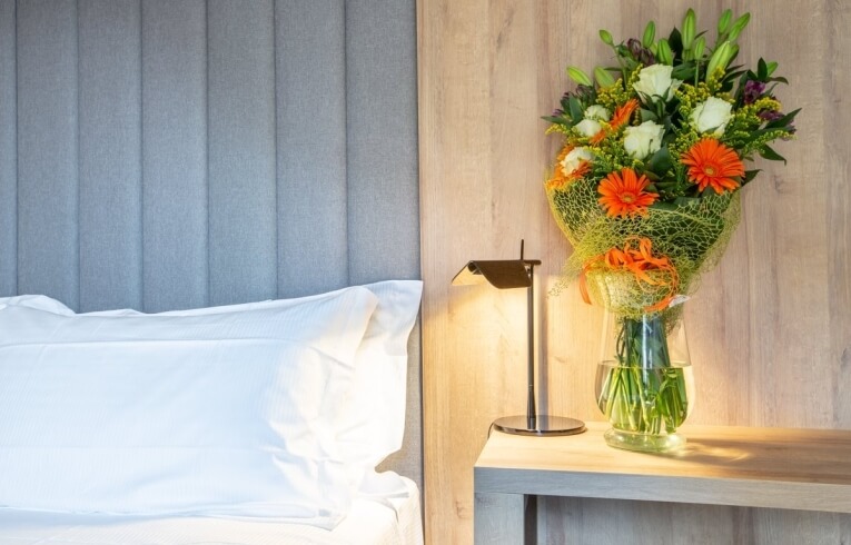 Bedside area with flowers, lamp, and gray headboard.