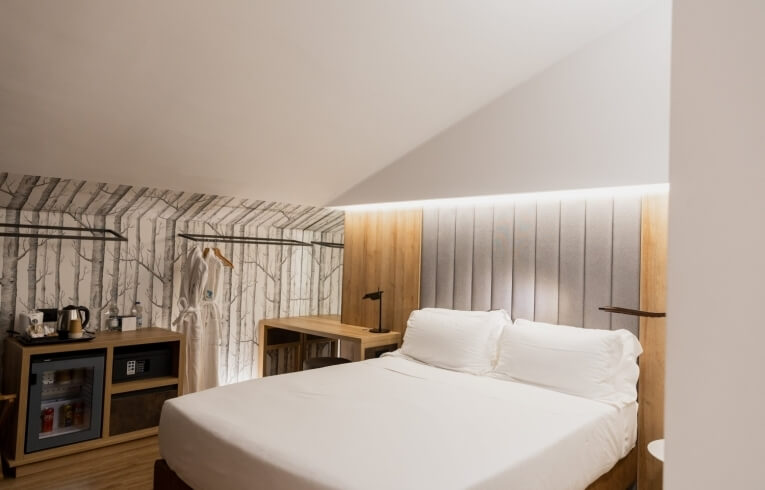 Cozy hotel room with a bed, desk, mini-fridge, and robes.