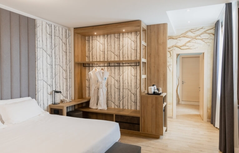 Cozy hotel room with bed, nightstand, closet, and birch tree wallpaper.