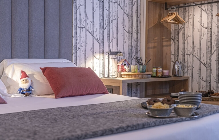 Cozy hotel room with bed, snacks, gnome, and decorative items.