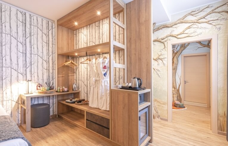 Hotel room with wooden closet, desk, mini fridge, and tree wallpaper.