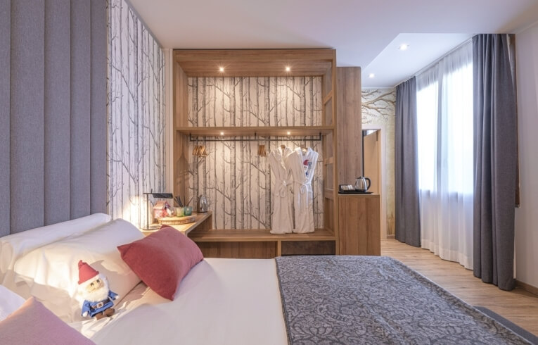 Hotel room with bed, wardrobe, kettle, and tree-patterned wall.