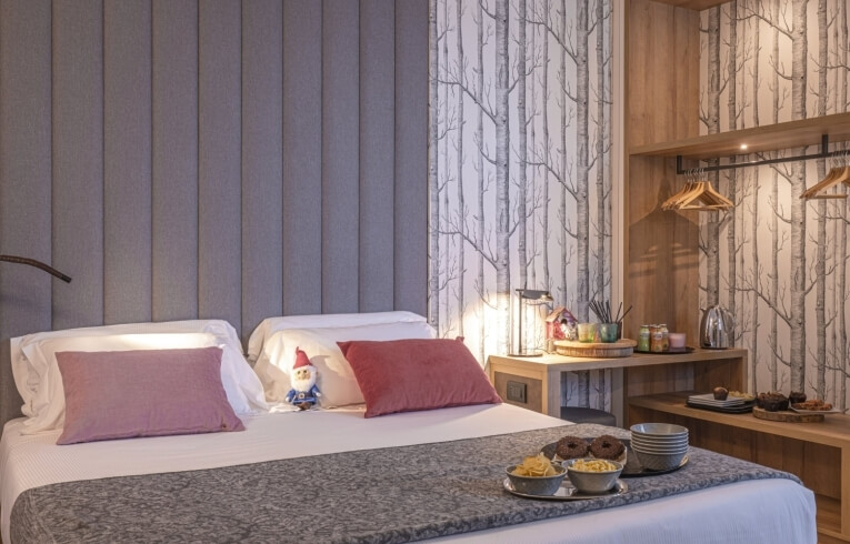 Cozy hotel room with a bed, gnome, nightstand, and tree-patterned wallpaper.