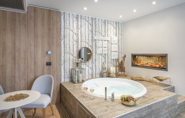Spa room with oval bathtub, wine glasses, and decorative elements.   Camera spa con vasca ovale, bicchieri di vino ed elementi decorativi.