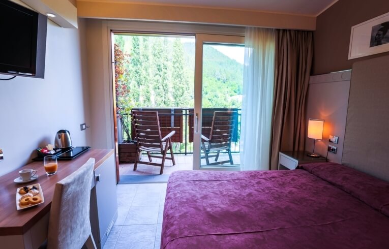 Hotelzimmer mit Bett, Schreibtisch, Balkon und Blick auf Bäume.