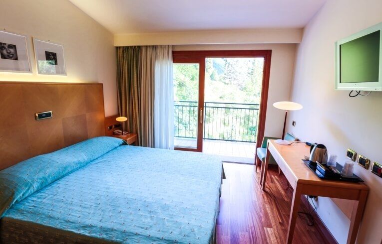 Camera d'hotel con letto, scrivania e balcone aperto.