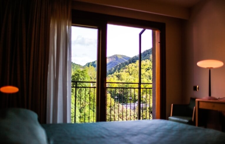 Camera d'hotel con vista su alberi e montagne, letto e scrivania.