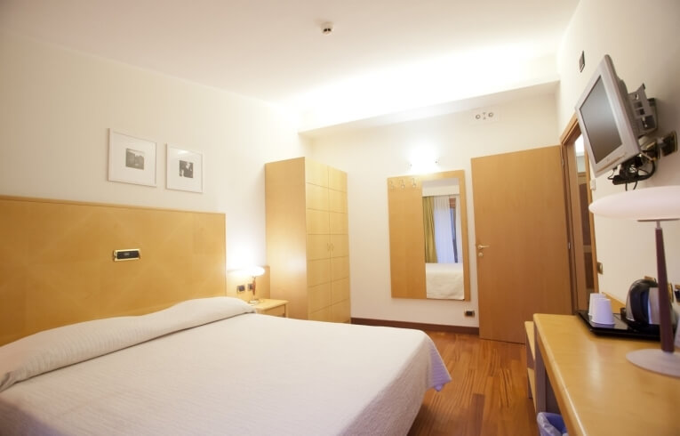 Camera d'hotel con letto, armadio, specchio e scrivania.