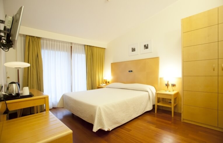 Camera d'hotel con letto, armadio, scrivania e TV montata.