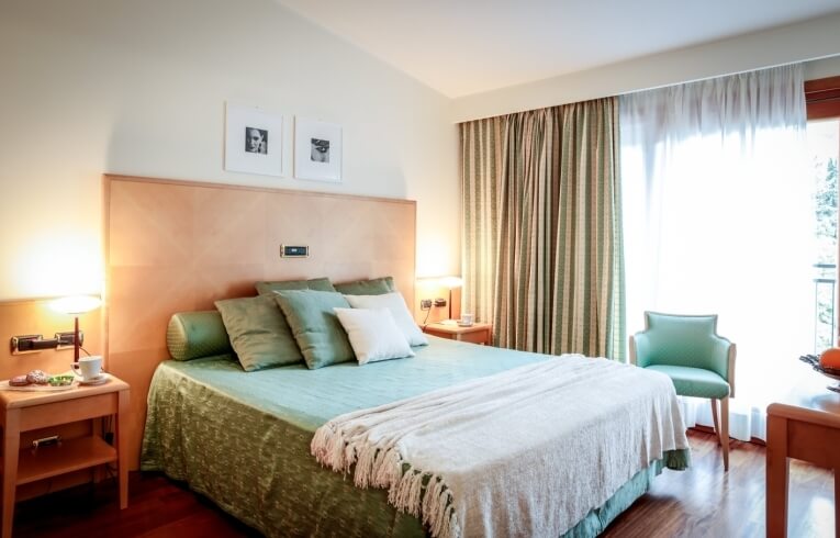 Camera d'hotel con letto verde, comodino e sedia teal.