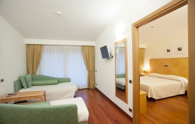 Camera d'hotel con soggiorno, letto, divani verdi e lampada.