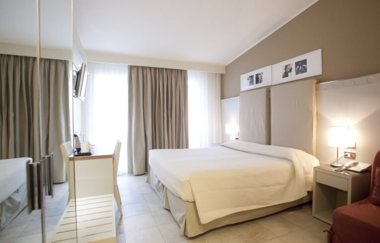 Hotel room with a large bed, desk, and large windows.