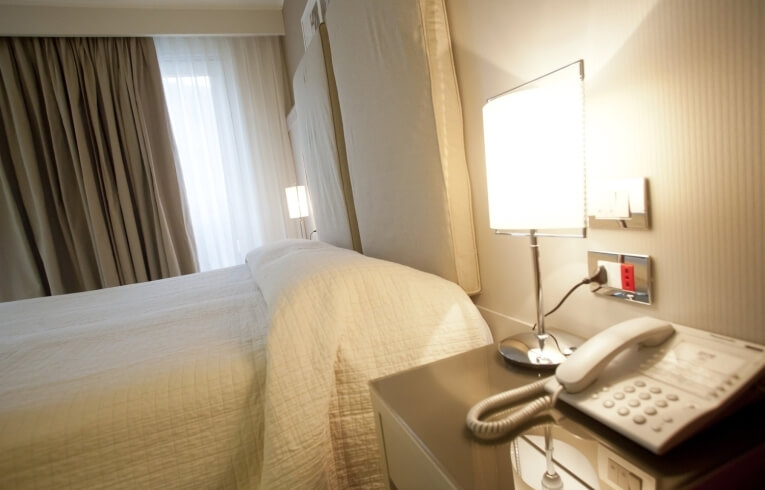 Hotel room with a bed, bedside table, and window curtains.