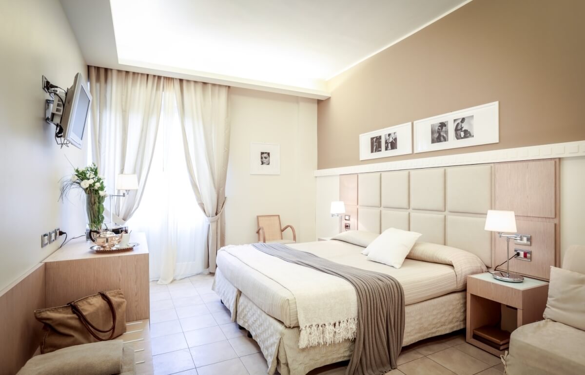 Camera d'hotel con letto grande, lampade, TV e fiori.