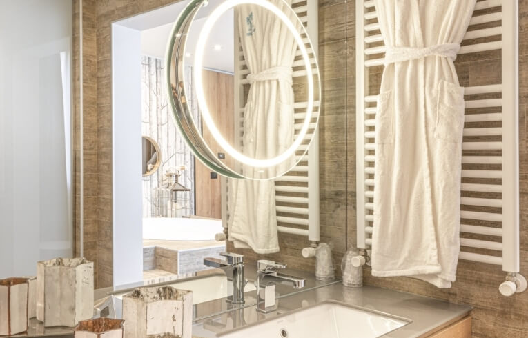 Bagno con lavabo, specchio circolare, accappatoio e pareti in piastrelle.