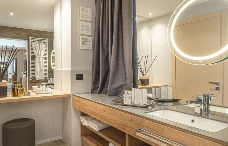 Bagno con vanity, specchio, asciugamani bianchi e prodotti per la cura.