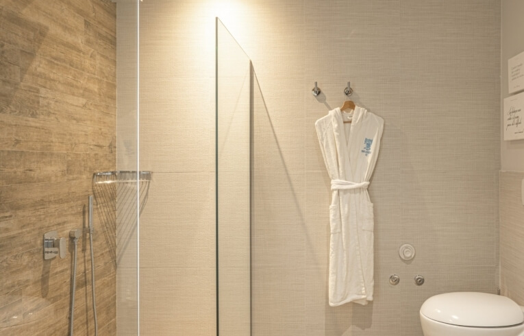 Accappatoio bianco appeso, doccia con pannello in vetro e WC.