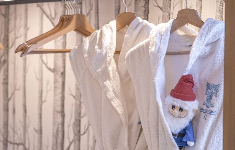 White bathrobes on hangers with a plush toy in one.