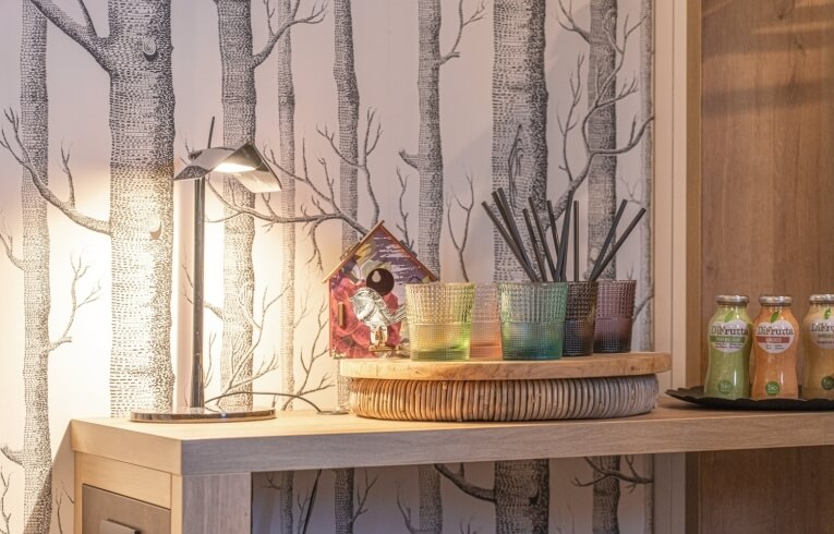 Illuminated desk lamp on shelf with glasses, birdhouse, and juice bottles.