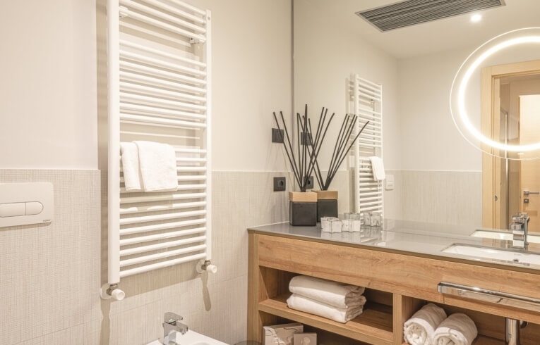 Hotel bathroom with towels, sink, mirror, and radiator.