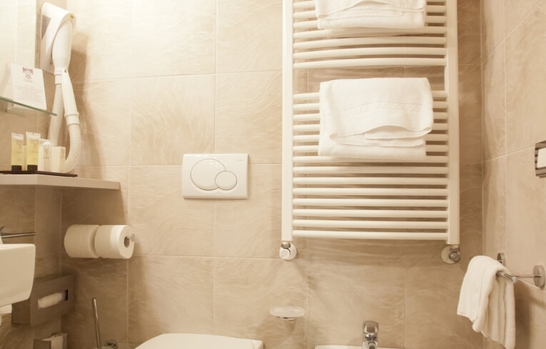 Beige tiled bathroom featuring a toilet, bidet, towels, and toiletries.