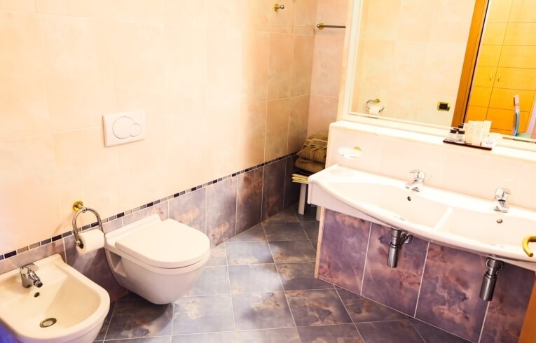 Bagno con toilet, bidet, doppio lavabo e specchio.