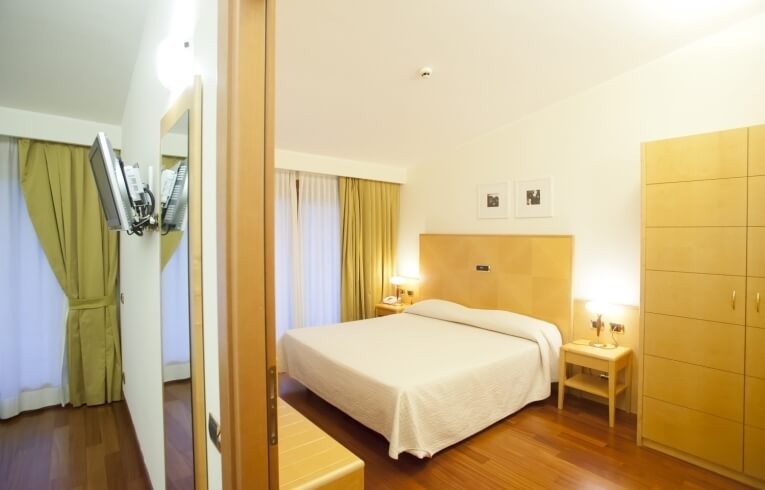 Camera d'hotel con letto, armadio, TV e tende gialle.
