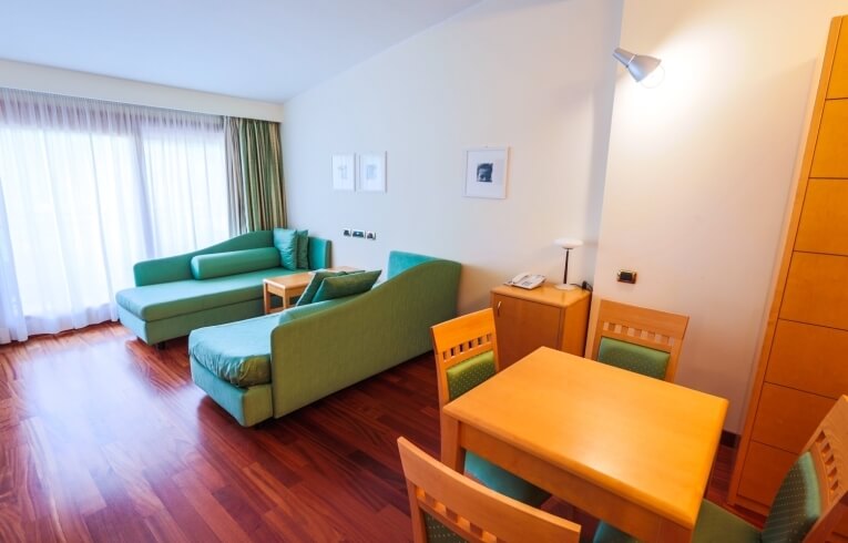 Camera d'hotel con tavolo, sedie verdi e chaise lounges.