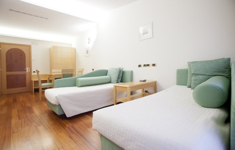 Camera d'hotel con due letti, tavolo e armadio in legno.