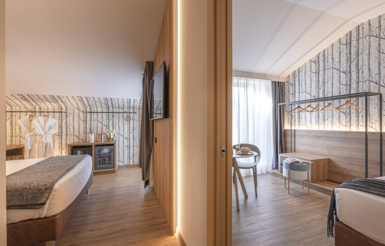 Hotel room with two beds, bathrobes, and tree-patterned wallpaper.