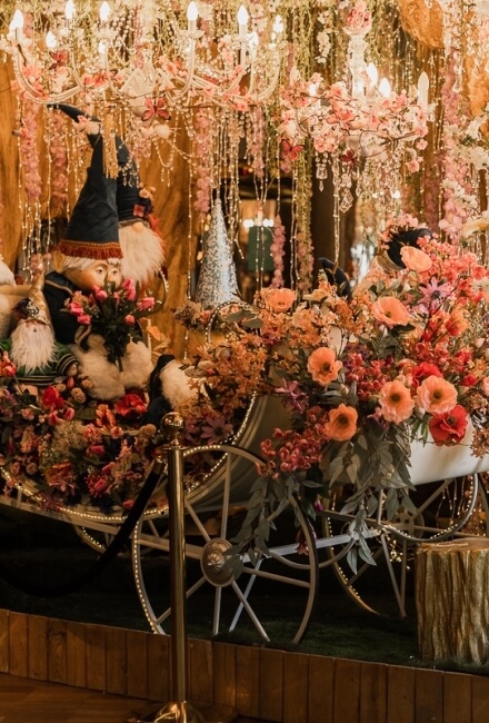 Esposizione di gnomi, carro, fiori colorati e luci decorative.