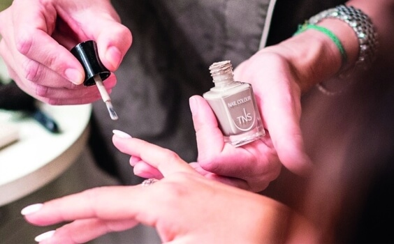 Nageltechnikerin lackiert Fingernägel einer Kundin mit "NAIL COLOUR TNS".