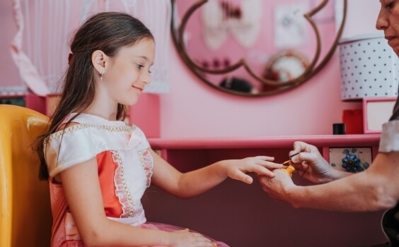 Bambina in abito da principessa mentre le si smaltiscono le unghie.