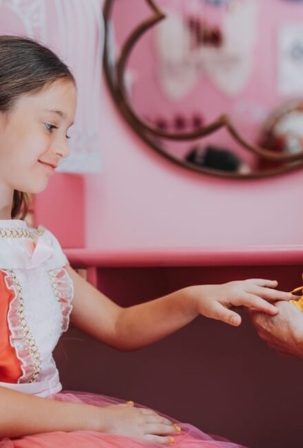 Bambina in abito rosa allunga la mano verso un oggetto giallo.