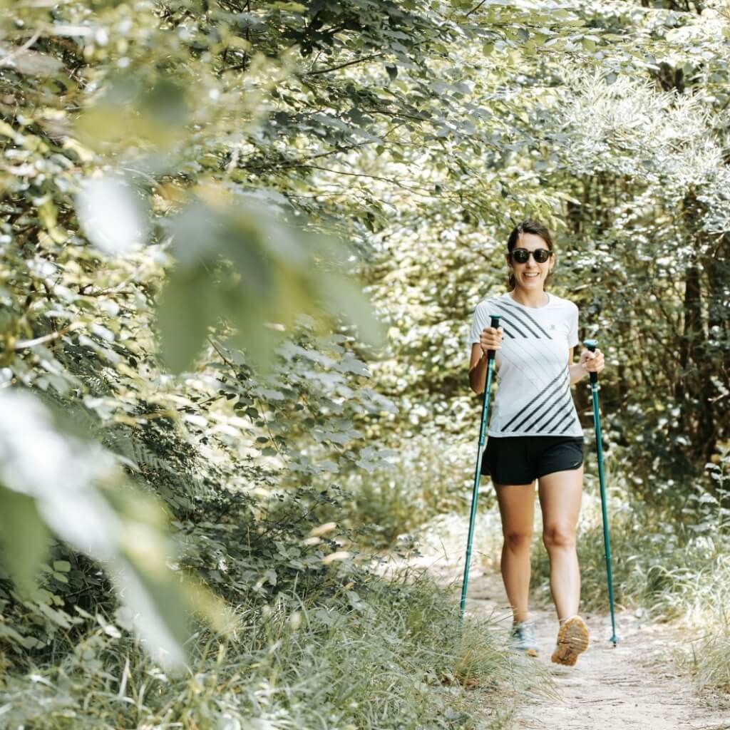Donna che cammina su un sentiero boschivo con bastoni da Nordic walking.