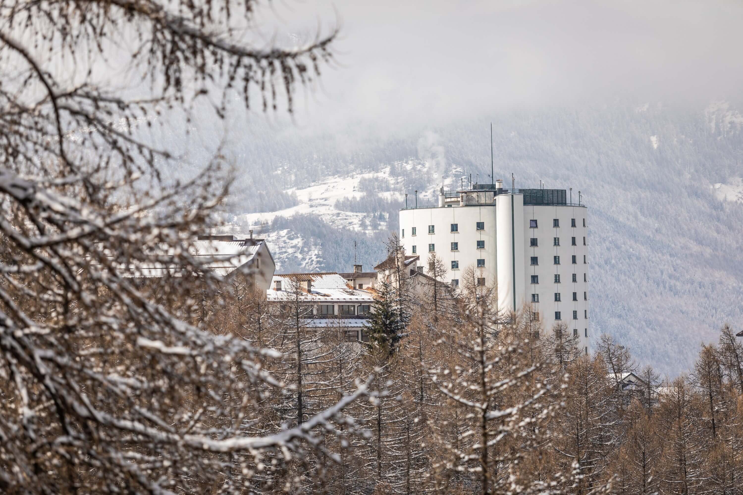 Majestic snow-covered mountain range with a prominent white building in the foreground and a cloudy sky above.