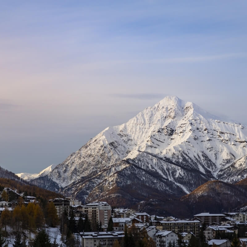 Montagna innevata con un villaggio ai piedi, cielo blu sereno e atmosfera tranquilla.